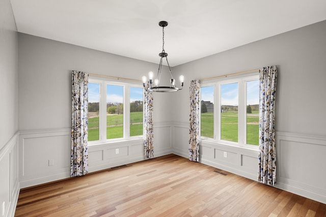 unfurnished dining area with a decorative wall, wainscoting, light wood-style flooring, and a notable chandelier