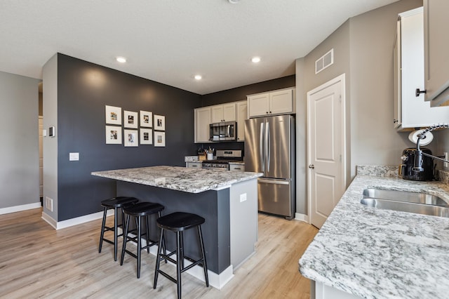 kitchen with appliances with stainless steel finishes, light wood-style floors, a breakfast bar area, a center island, and visible vents
