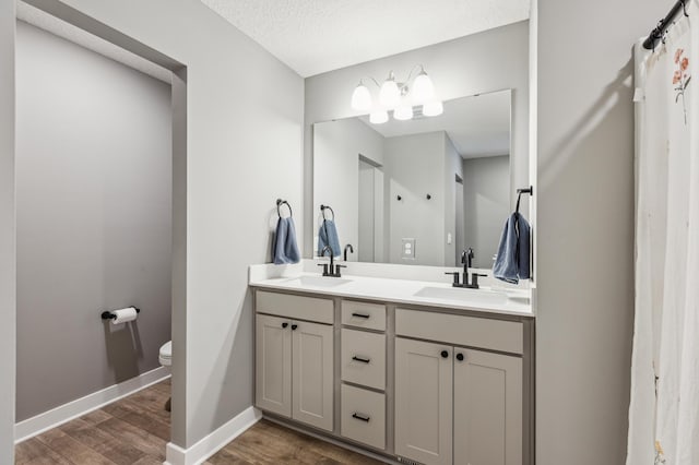 full bath with double vanity, a sink, wood finished floors, and toilet