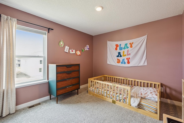 carpeted bedroom with a nursery area, a textured ceiling, visible vents, and baseboards