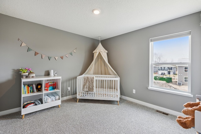 carpeted bedroom featuring visible vents, a textured ceiling, a crib, and baseboards
