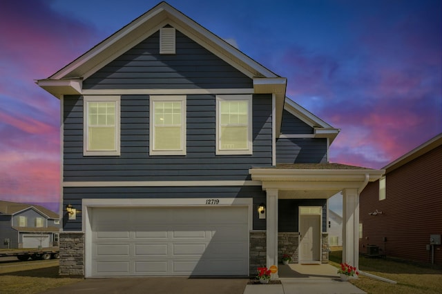 traditional home featuring central AC unit, an attached garage, driveway, and stone siding