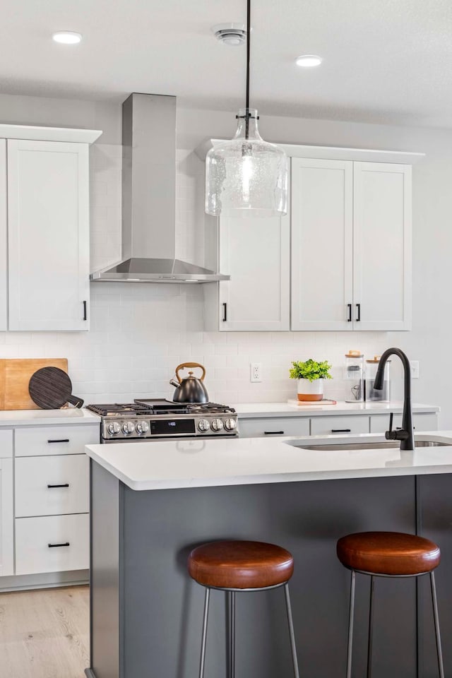 kitchen with light countertops, a breakfast bar, stainless steel gas stove, and wall chimney range hood
