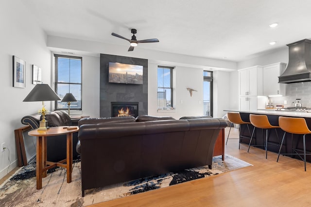 living area with light wood-style flooring, a large fireplace, a ceiling fan, plenty of natural light, and recessed lighting