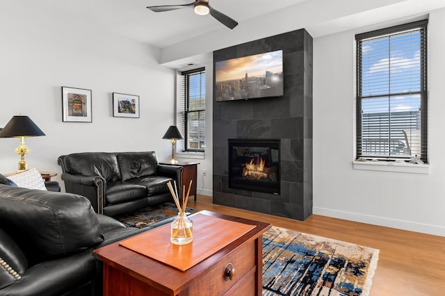 living room featuring baseboards, ceiling fan, wood finished floors, and a tile fireplace