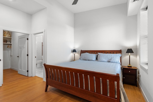 bedroom with wood finished floors, baseboards, ensuite bathroom, a ceiling fan, and a spacious closet
