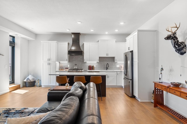 kitchen featuring premium range hood, freestanding refrigerator, a sink, light wood-style floors, and tasteful backsplash