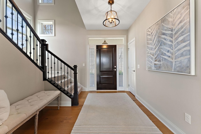 foyer featuring an inviting chandelier, baseboards, wood finished floors, and stairway