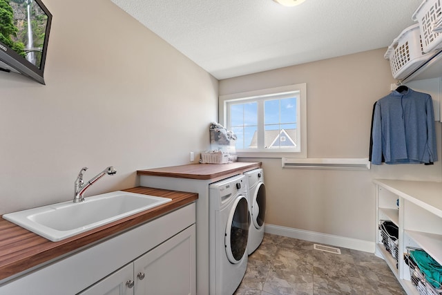 washroom with visible vents, cabinet space, a sink, baseboards, and washer and clothes dryer