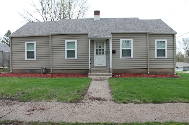 ranch-style home with a chimney, a shingled roof, and a front yard