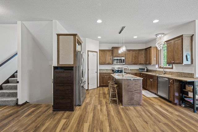 2895 Thunder Bay Ct, Little Canada, MN 55117 - kitchen with appliances with stainless steel finishes, a sink, dark wood-style floors, a center island with sink, and light stone counters