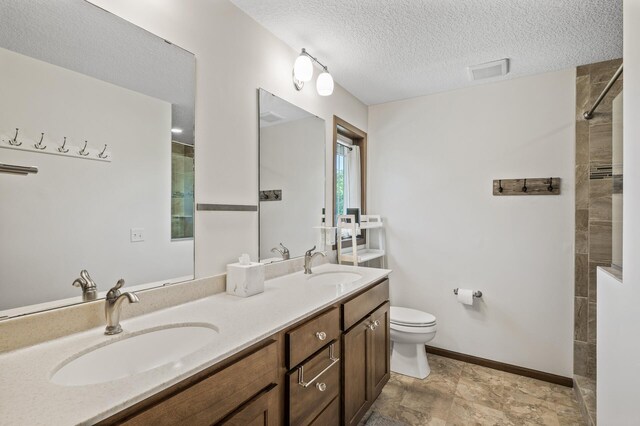 2895 Thunder Bay Ct, Little Canada, MN 55117 - bathroom featuring toilet, a tile shower, a textured ceiling, double vanity, and baseboards