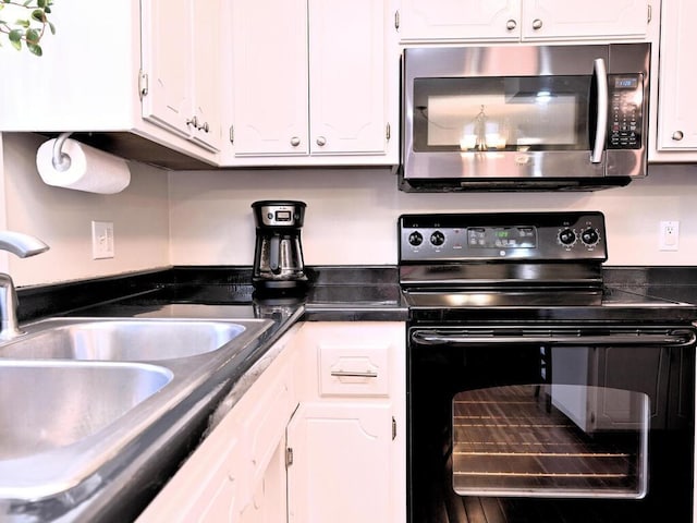 kitchen with stainless steel microwave, a sink, white cabinetry, electric range, and dark countertops