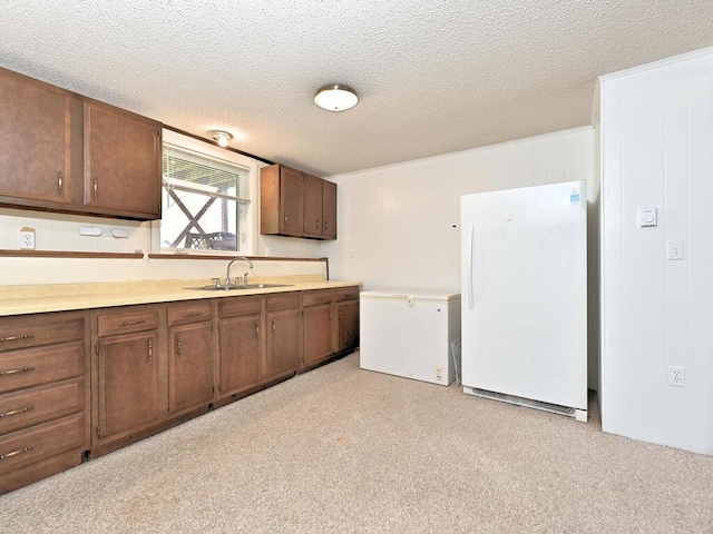 kitchen with a sink, fridge, freestanding refrigerator, a textured ceiling, and light countertops