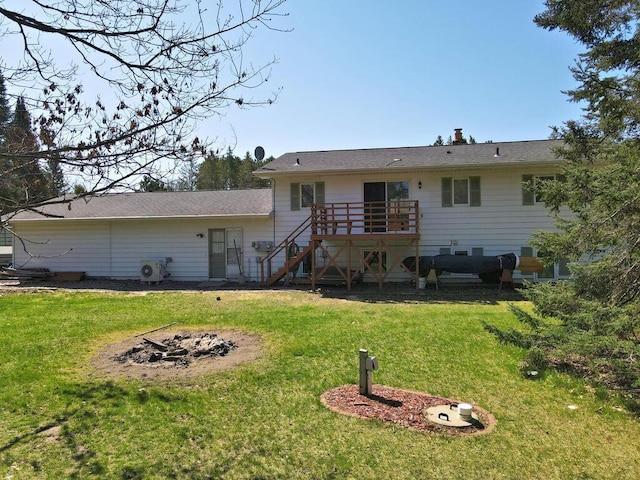 rear view of house with stairs, a wooden deck, a fire pit, and a lawn