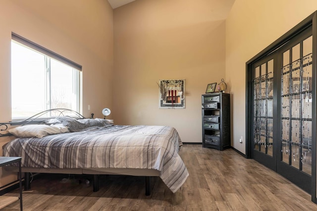 bedroom with wood finished floors, baseboards, and a high ceiling