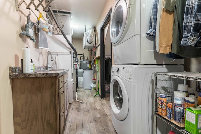 clothes washing area featuring a sink, stacked washer / drying machine, light wood-type flooring, and laundry area