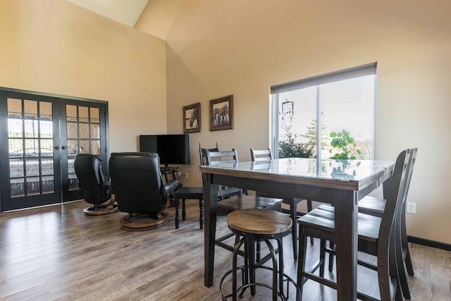 dining space with baseboards, high vaulted ceiling, french doors, and wood finished floors