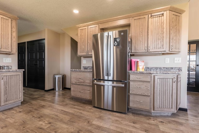 kitchen with freestanding refrigerator, wood finished floors, light stone countertops, recessed lighting, and a textured ceiling