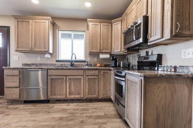 kitchen featuring light wood-style floors, recessed lighting, dark stone counters, a sink, and appliances with stainless steel finishes