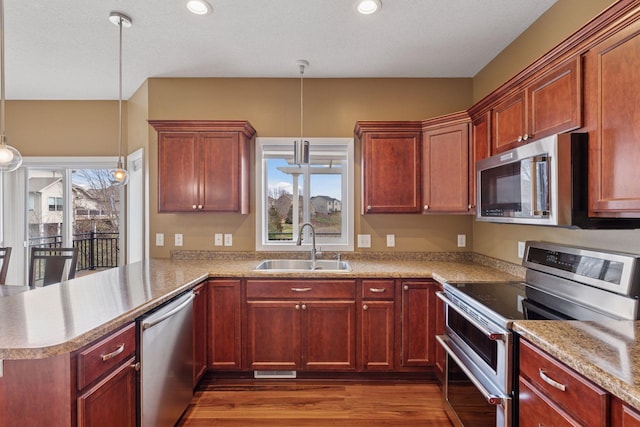 kitchen with pendant lighting, dark wood finished floors, a sink, a peninsula, and stainless steel appliances