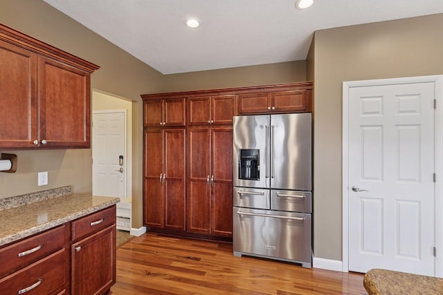 kitchen with recessed lighting, light stone counters, high end refrigerator, and wood finished floors