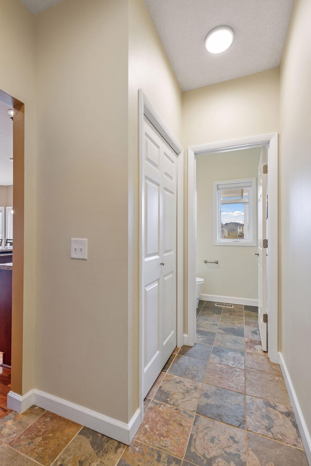 hall with baseboards, visible vents, and stone tile flooring