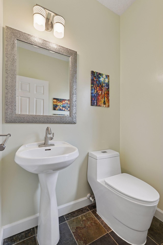 half bathroom with toilet, baseboards, and a sink