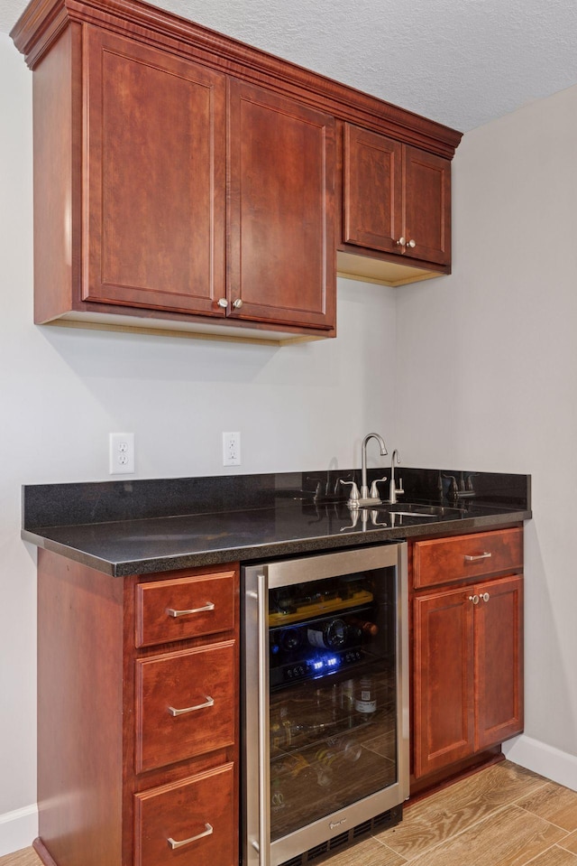 bar featuring light wood finished floors, a sink, baseboards, wet bar, and wine cooler