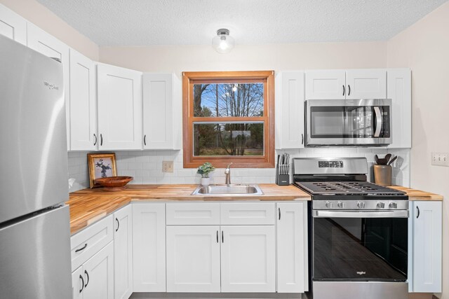 23245 County Rd W, Grantsburg, WI 54840 - kitchen with butcher block countertops, stainless steel appliances, a sink, tasteful backsplash, and a textured ceiling