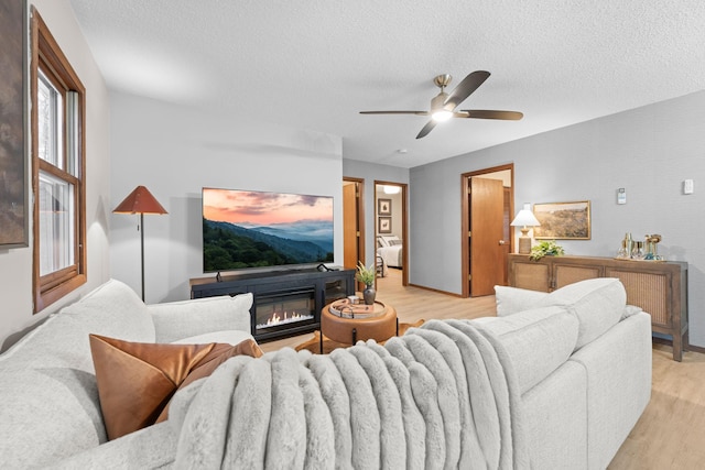 23245 County Rd W, Grantsburg, WI 54840 - living area featuring light wood-style flooring, a textured ceiling, ceiling fan, a glass covered fireplace, and baseboards