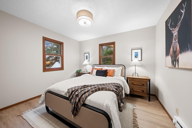 23245 County Rd W, Grantsburg, WI 54840 - bedroom featuring a baseboard radiator, light wood-style floors, baseboards, and a textured ceiling
