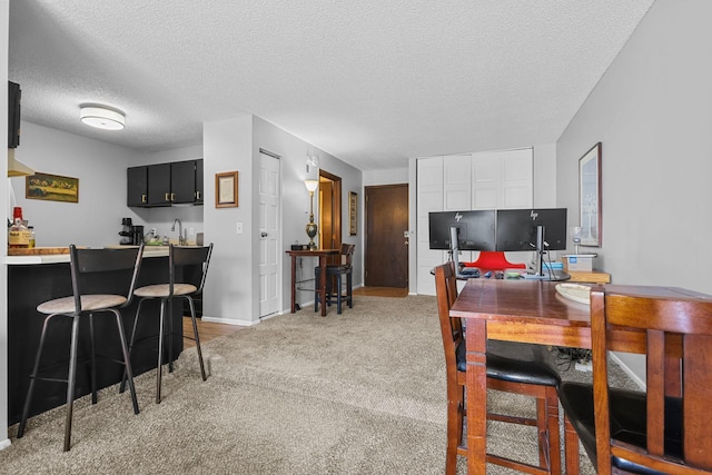 dining space with light colored carpet, a textured ceiling, and wet bar
