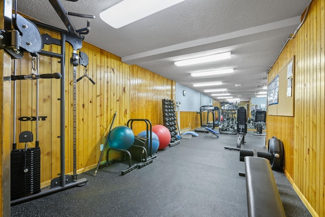 gym featuring wooden walls, baseboards, and a textured ceiling