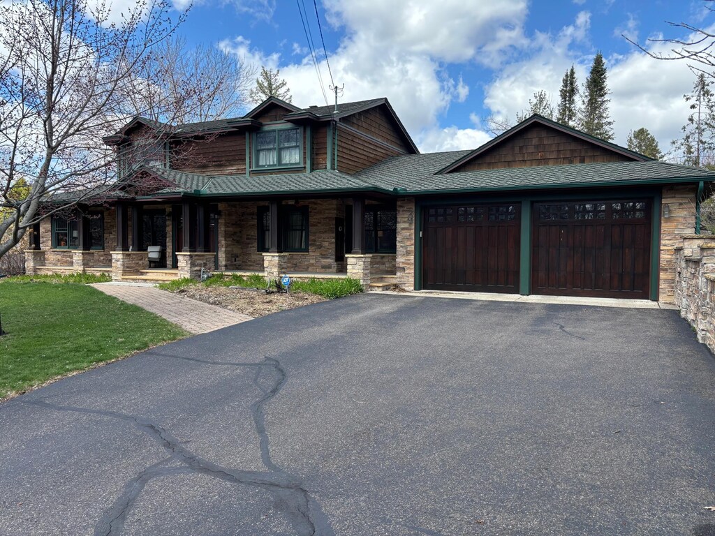 view of front of home featuring a garage, a front lawn, stone siding, a porch, and driveway