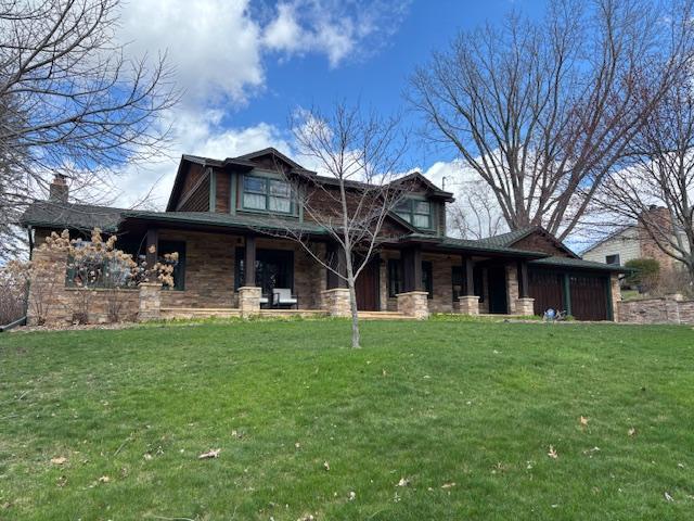view of front facade with an attached garage, a front yard, covered porch, and stone siding