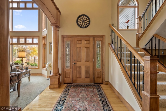 foyer entrance with a high ceiling, decorative columns, baseboards, and light wood-style floors