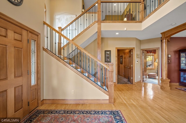 entrance foyer featuring wood finished floors, stairway, baseboards, a high ceiling, and ornate columns