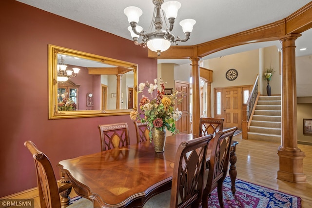dining area with stairs, decorative columns, wood finished floors, and a chandelier