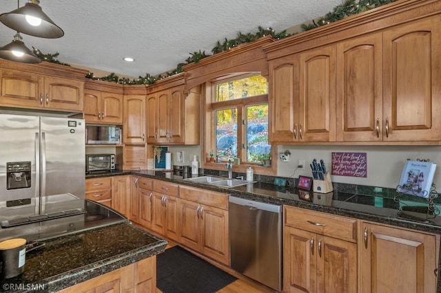 kitchen with appliances with stainless steel finishes, a sink, a textured ceiling, brown cabinetry, and a toaster