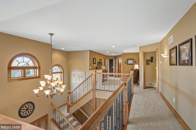 hall with light colored carpet, a notable chandelier, an upstairs landing, and visible vents