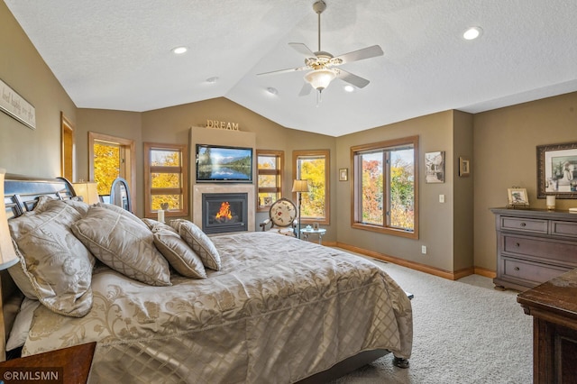 bedroom featuring carpet floors, a glass covered fireplace, baseboards, a textured ceiling, and vaulted ceiling