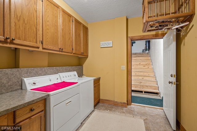 laundry area with baseboards, a textured ceiling, cabinet space, and washer and dryer