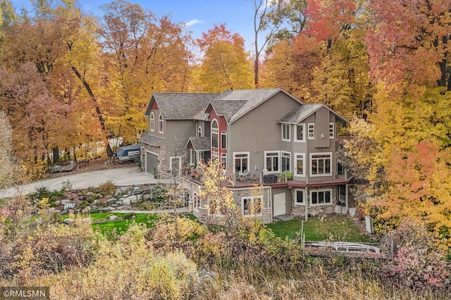 back of property with a garage, concrete driveway, and stone siding