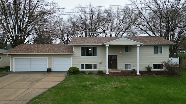raised ranch with fence, a front yard, roof with shingles, concrete driveway, and an attached garage