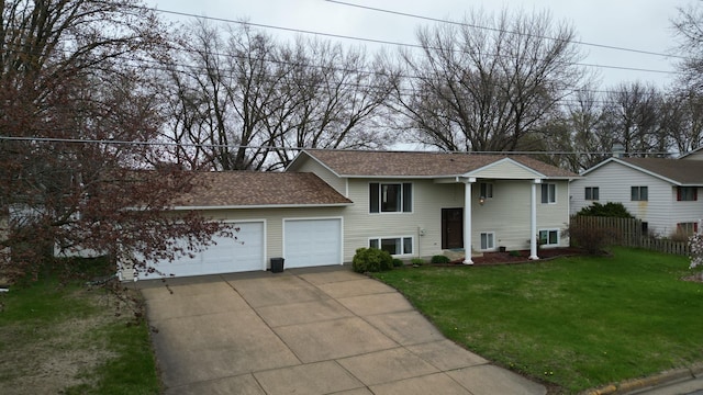 raised ranch with fence, roof with shingles, a front lawn, a garage, and driveway