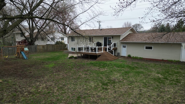 rear view of property featuring a lawn, a deck, fence, and roof with shingles