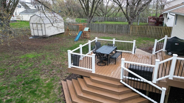 wooden terrace with outdoor dining area, a storage shed, an outbuilding, a fenced backyard, and a playground