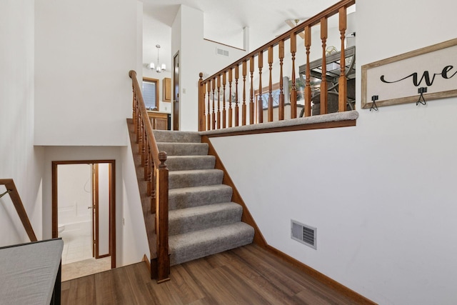 staircase with a high ceiling, visible vents, and wood finished floors