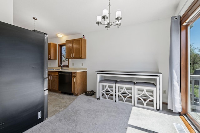 kitchen with brown cabinets, hanging light fixtures, an inviting chandelier, freestanding refrigerator, and black dishwasher